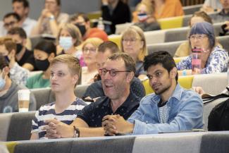 Three people sitting in a lecture theatre and smiling at something off camera