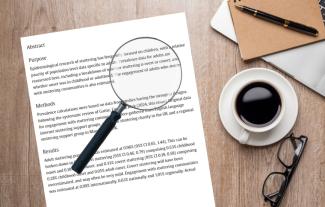 A piece of paper on a desk with text on it. On top of the paper is a magnifying glass, and a cup of coffee is next to it