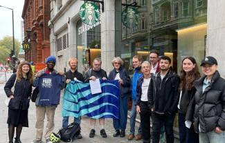 A group of people standing outside a coffee shop. Some are holding a flag