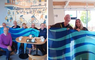 A group sitting in a coffee shop and smiling, holding a flag, and a man and woman smiling and holding a flag