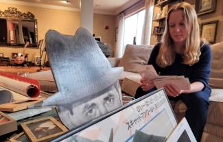 A woman sitting on a sofa, going through a set of photographs, with various items of memorabilia in front of her