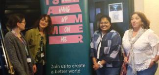 Four women standing beside an information banner