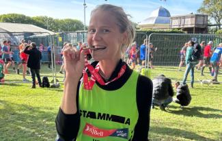 A young woman in a running vest biting a medal that's round her neck