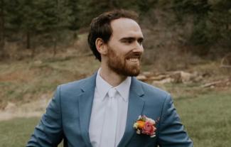 A man in a wedding suit looking to the right and smiling