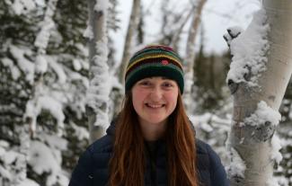 A young woman smiling against a snowy forest scene