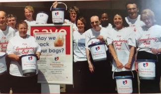 A group of people in matching t-shirts holding fundraising buckets and smiling