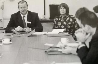 A man and a woman sitting at a conference desk in smart clothes