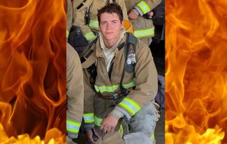 A man in a firefighter's uniform kneeling and looking at the camera.