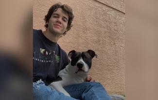 A young man smiling, with a dog on his lap