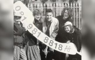 A group of adults and children smiling and holding up a banner with a phone number on it
