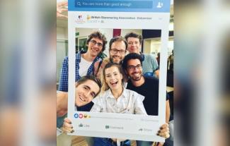 A group of young people holding up a large frame and posing for the camera