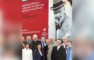 A group of people smiling and standing in front of a billboard