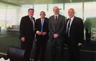 Four men in suits standing in an office and smiling
