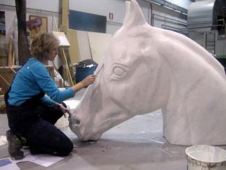 A woman painting a horse's head piece of art