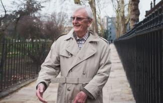 A man in a raincoat in a park setting, smiling