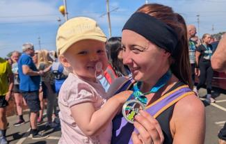 A mother in running gear cuddling her baby daughter and holding up a medal
