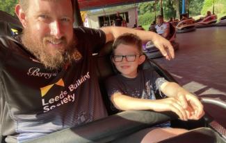 A man and his son sitting in a bumper car and smiling