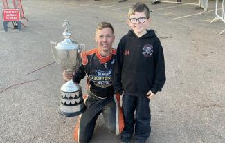A racing driver holding a trophy, posing with a young boy and smiling