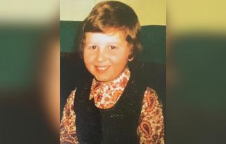 A young boy in 1970s clothes, smiling