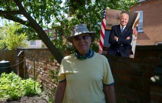 A man wearing a hat and sunglasses, standing in a garden, beside an image of President Joe Biden