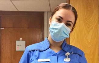 A nurse wearing a facemask looking at the camera and tilting her head
