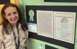 A girl standing next to a drawing on a noticeboard and smiling