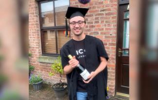 A young man in graduation robes holding a bottle of champagne