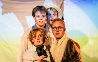 Four actors huddled together on a stage and looking at the camera, in character