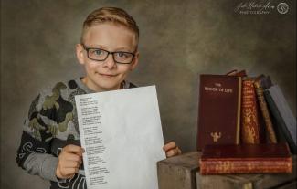 A young boy holding up a piece of paper with a poem typed on it