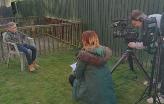 A film crew in a garden filming a young boy sitting on a garden chair