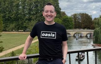 A man standing on a bridge over a river, smiling