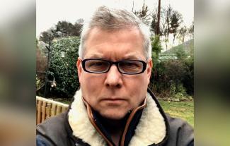 A man wearing glasses in a garden looking at the camera