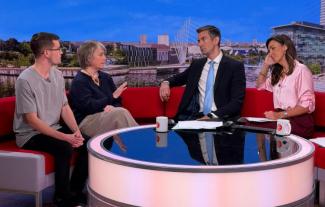 Four people sitting on a sofa in a tv studio, a man and a woman on the left, speaking to another man and woman on the right