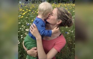 A mother holding her young son in a meadow surrounded by flowers
