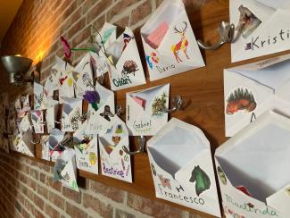 Rows of envelopes stuck to a wall, each one decorated and containing notes and objects