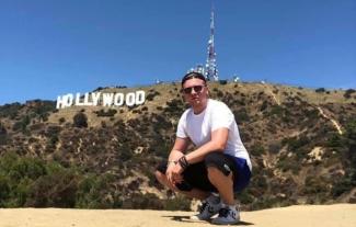 A man squatting in front of the Hollywood sign