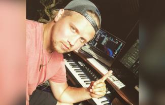 A man in front of a computer and keyboard, smiling and pointing up