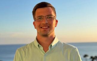 A young man smiling with the ocean behind him