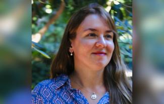 A woman smiling and looking to the right, in front of a tree