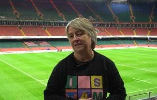 A woman standing in the seated area in a sporting stadium, with the pitch behind her