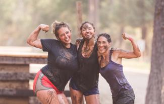Three women covered in mud posing together after a running event