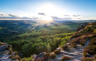 An aerial view of the hills and valleys of the Peak District in Derbyshire, with the sun peaking through clouds