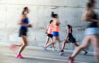 Women running in an urban setting, with one doing stretches