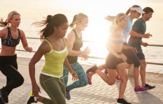 A group of runners, male and female, running next to the coast, with the sun shining behind them