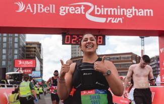 A woman posing at the end of a sponsored run, smiling with her thumbs up