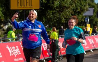 A man and woman running in a sponsored run. The man is holding a phone and taking a selfie