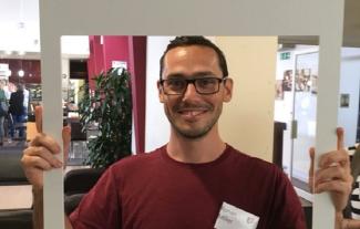 A man looking through a cardboard frame and smiling