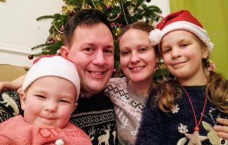 A mother and father posing with their two children in front of a Christmas tree