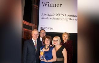 Two men and three women, one of the women holding an award, smiling at an awards ceremony