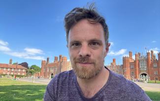A man smiling, with Hampton Court Palace in the background